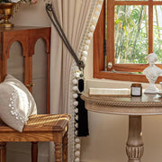 Beige curtain with decorative trim beside a wooden window and vintage-style furniture