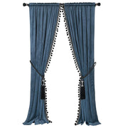 Slate blue velvet curtains with black pom-pom trim and decorative tiebacks framing a window
