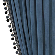 Close-up of slate blue velvet curtain folds with black pom-pom trim