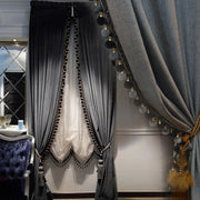 Charcoal grey velvet curtains with black pom-pom trim and decorative tiebacks framing a window