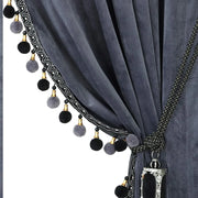 Charcoal grey velvet curtain with curved black pom-pom trim and decorative tassel tieback