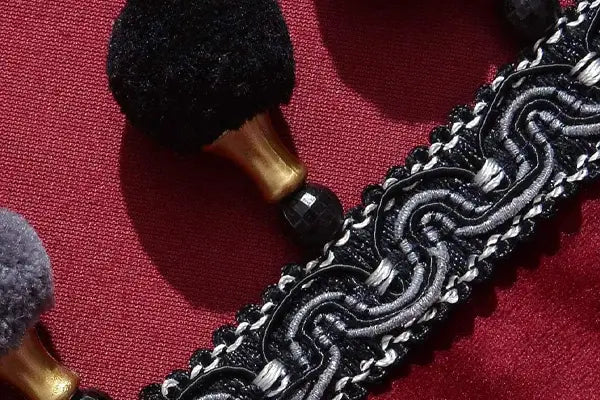 Close-up of black pom-pom trim with gold tassel caps and woven braid on red fabric