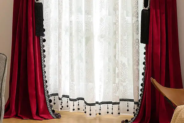 Red velvet curtains with pom-pom trim and tassel tiebacks layered over white lace sheer curtains