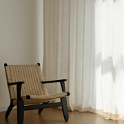 Warm ivory floor-length curtains beside a wooden lounge chair in a softly lit interior