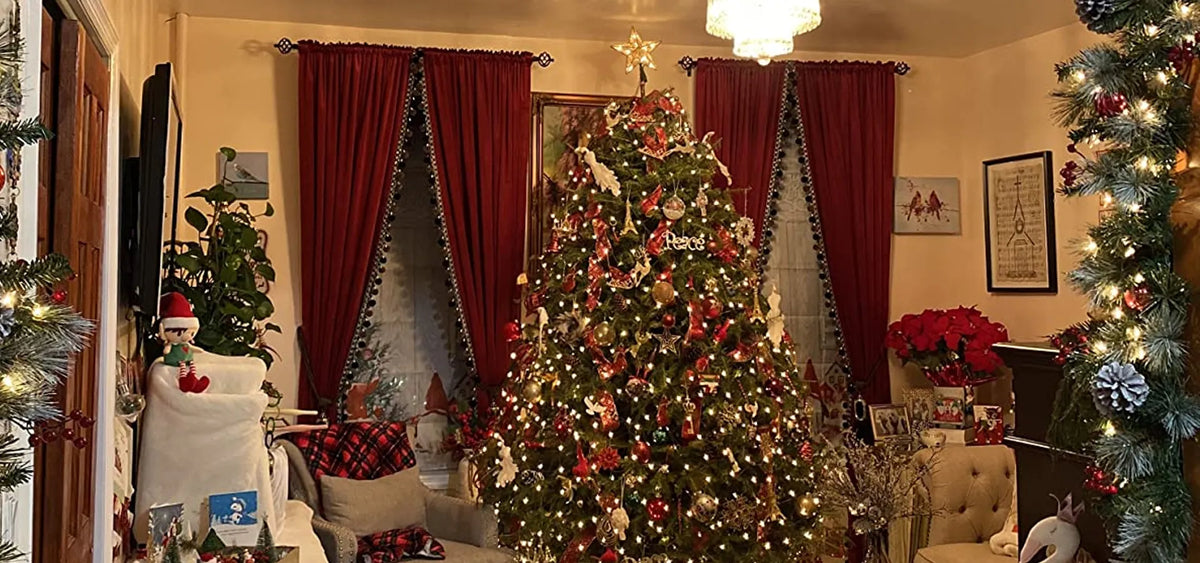 Burgundy velvet curtains with black pom pom trim framing windows in a cozy Christmas living room