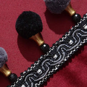 Close-up of burgundy velvet curtain with black embroidered trim and decorative pom-pom tassels