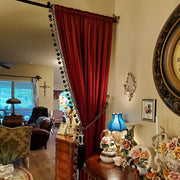 Burgundy velvet curtain with black pom-pom trim and decorative tieback in a vintage-style living room