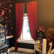 Burgundy velvet curtains with black pom-pom trim elegantly draped around a bedroom window