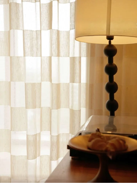 Patterned sheer curtain beside a warm table lamp