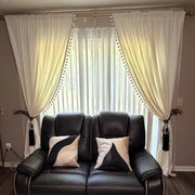 Beige curtains framing a living room window above a black leather sofa