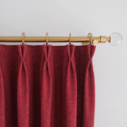 Close-up of burgundy linen-look curtains with pleated headers hanging from a wooden curtain rod