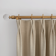 Close-up of oatmeal linen-look curtains with pleated headers hanging from a wooden curtain rod
